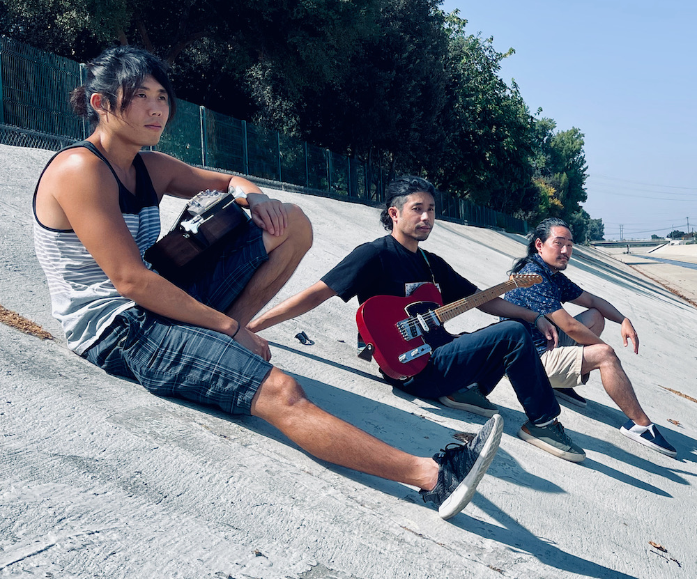 Tat, Aki and Wes sitting with their instruments in a concrete canal in Long Beach